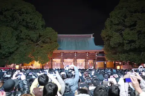 A large crowd at a shrine at night during New Year hatsumode, many holding up phones