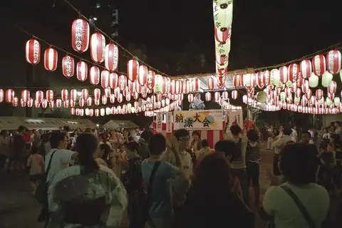 Red and white paper lanterns strung above a crowd at a Bon Odori festival, with a stage in the distance