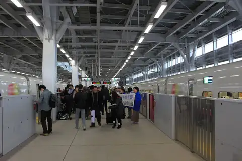 Passengers with suitcases on a platform at Shin-Aomori Station, with white Shinkansen trains on both sides