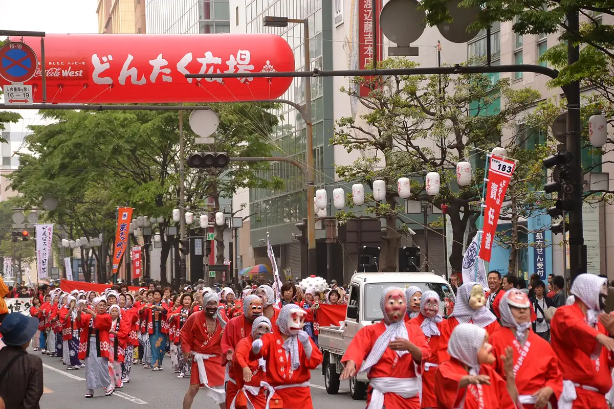 Performers in red costumes and white headscarves march down a street during the Hakata Dontaku parade