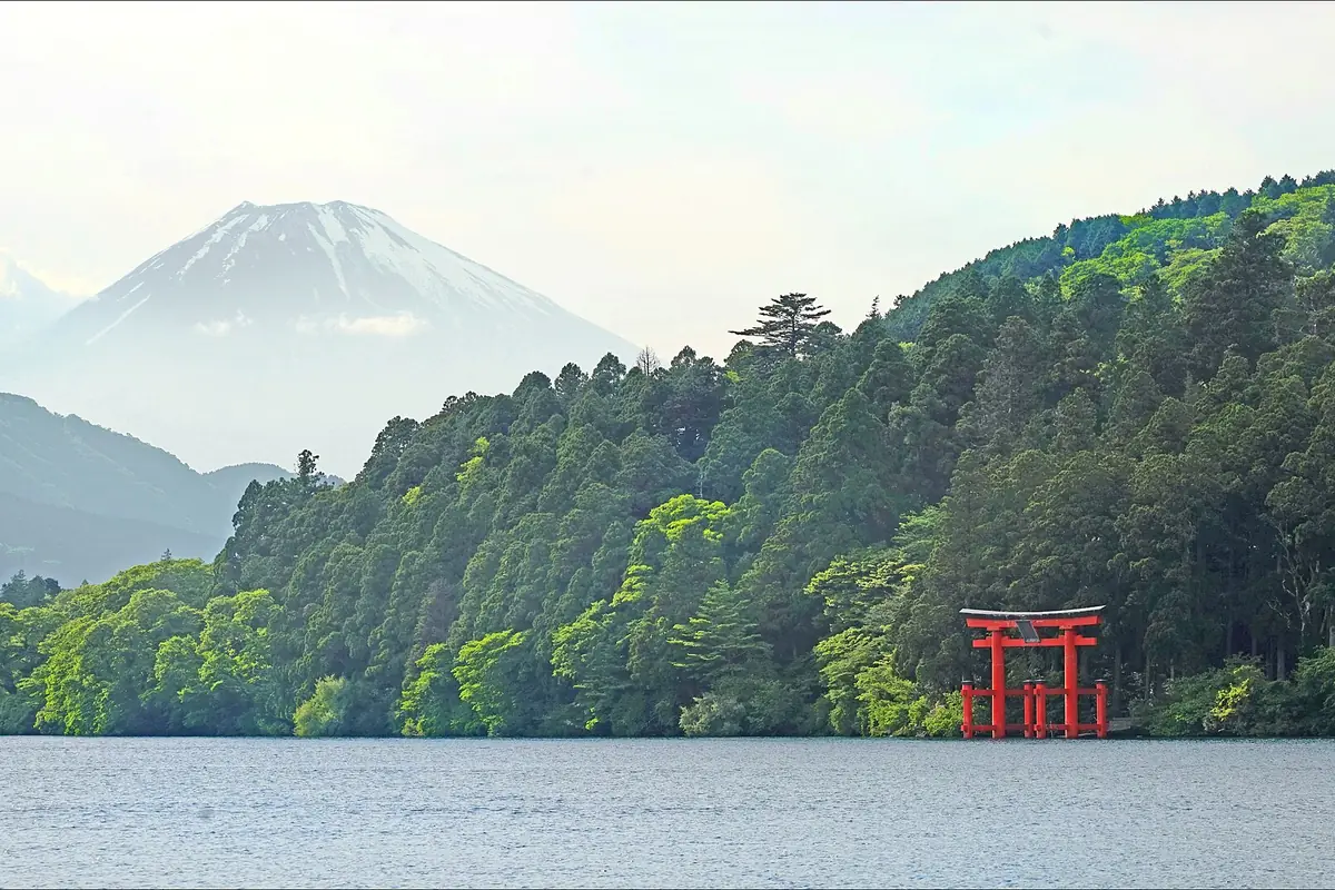Lake Ashi in Hakone with snow-capped Mount Fuji in the distance and a red torii gate of Hakone Shrine on the shore