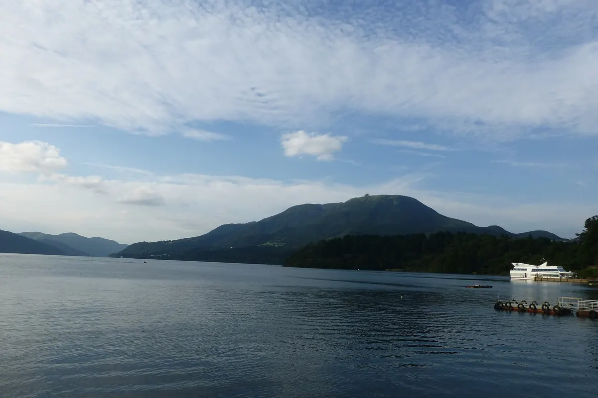 Calm water of Lake Ashi in Hakone, with forested mountains behind and a white boat moored at a pier