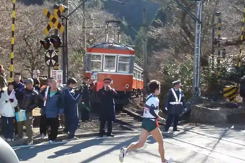 하코네 에키덴 선수가 주황색 하코네 등산열차와 관중 앞 선로를 가로지르는 모습