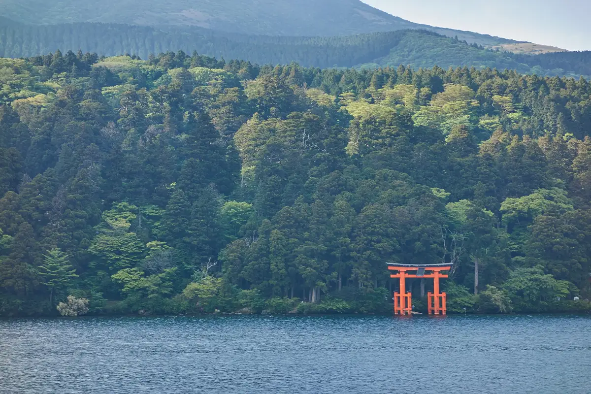 The red torii gate of Hakone Shrine standing in Lake Ashi, with a forested hillside behind it