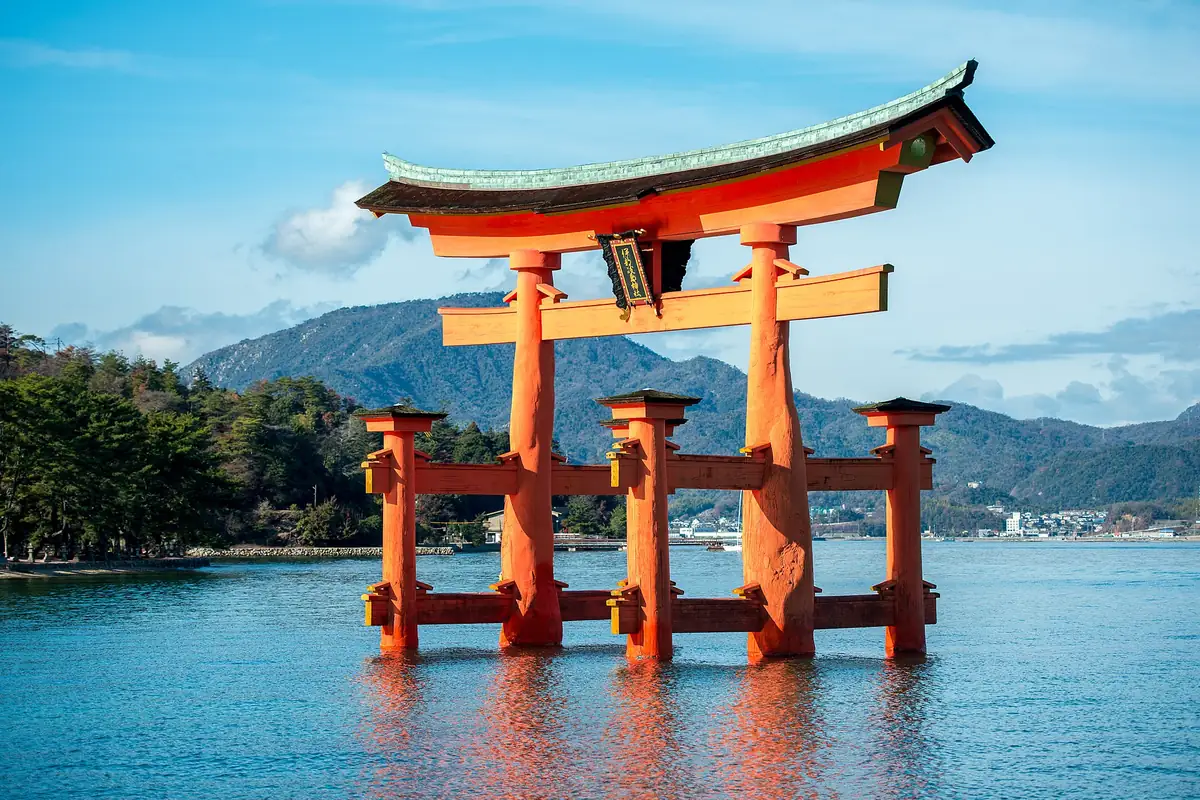 The red torii gate of Itsukushima Shrine standing in the sea at Miyajima, with mountains behind