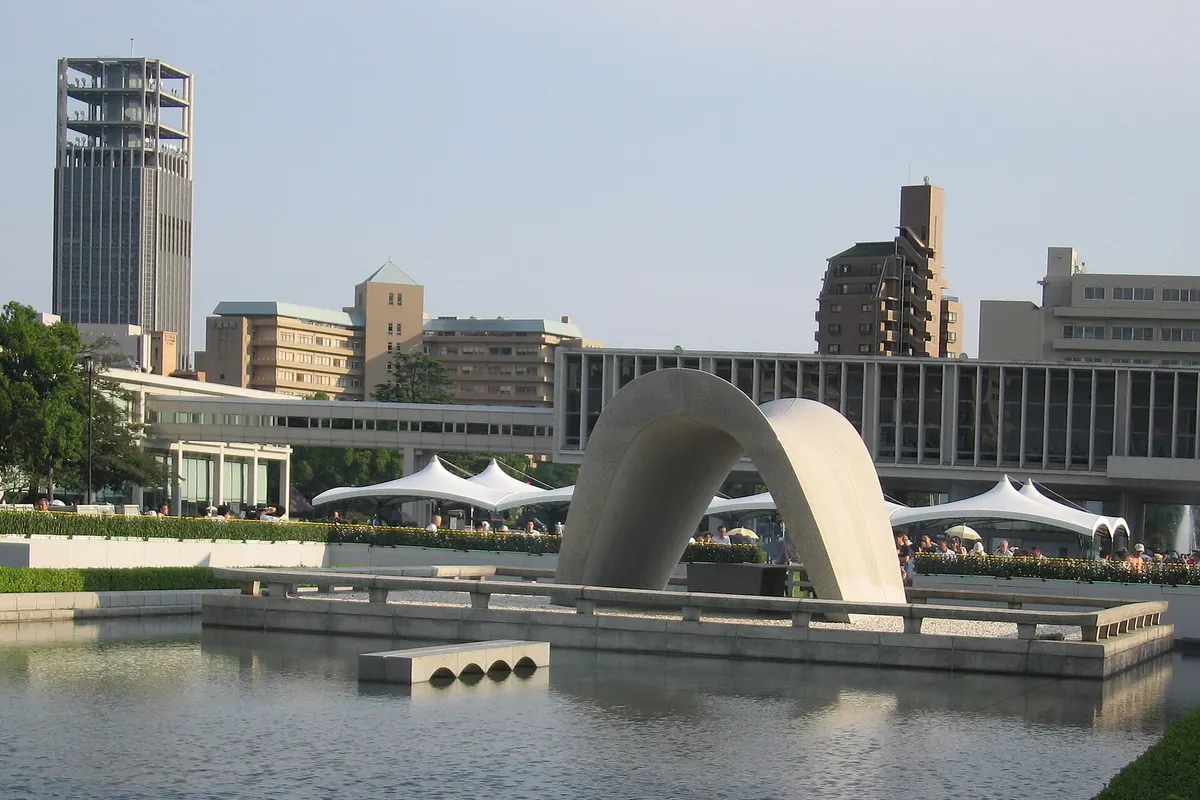 平和記念公園のアーチ型の原爆死没者慰霊碑が池に映る様子、背後に白いテント