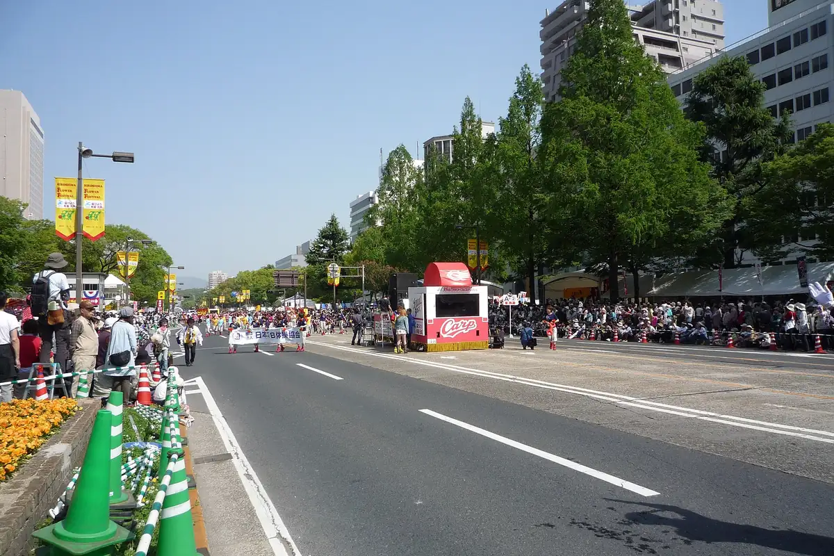 Crowds lining a tree-lined boulevard watching a parade during the Hiroshima Flower Festival