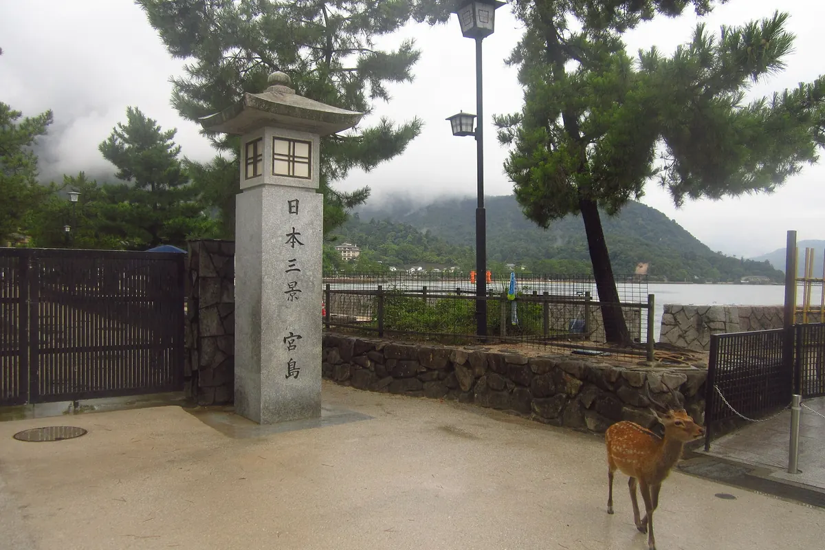 A stone lantern marking Miyajima as one of the Three Views of Japan, with a deer nearby and the sea behind