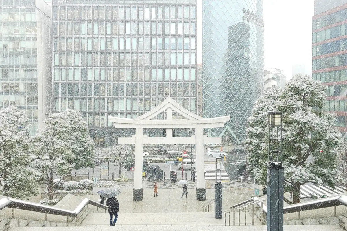 Torii gate of Hie Shrine in falling snow with Tokyo office towers in the background