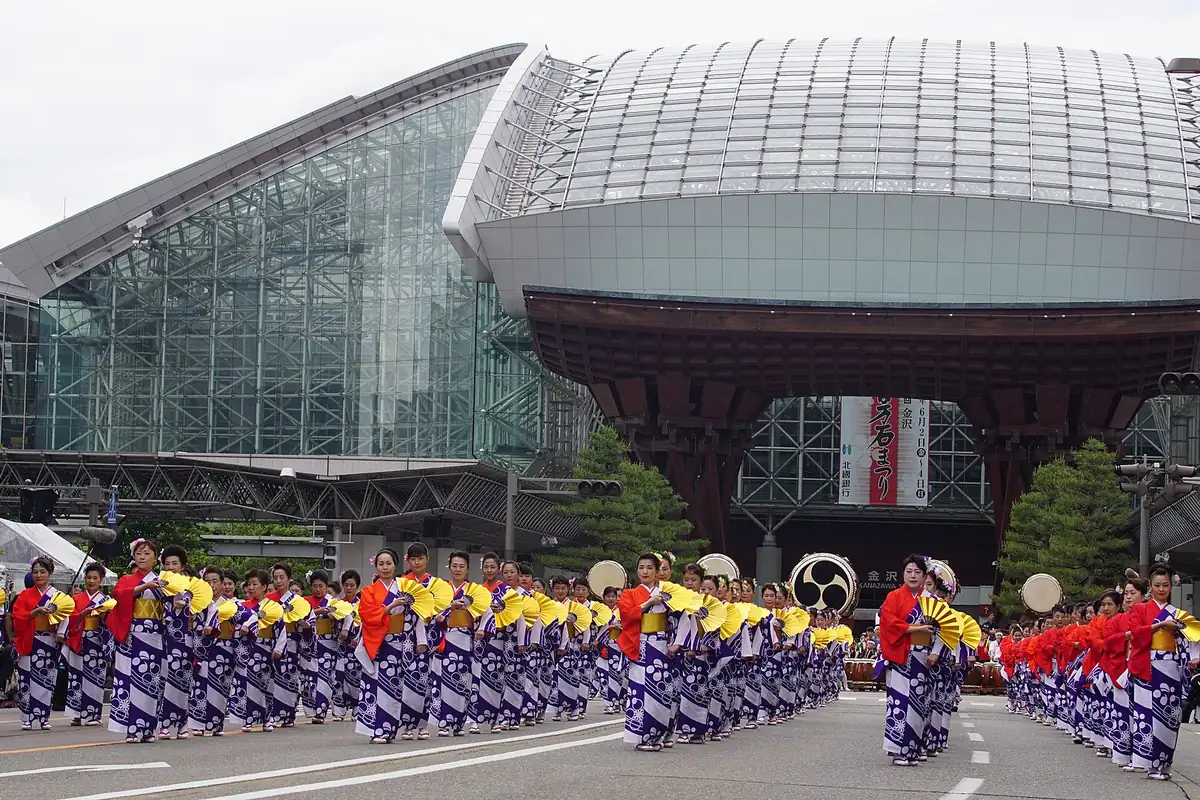Rows of dancers in matching yukata with yellow fans parading in front of Kanazawa Station during the Hyakumangoku Festival