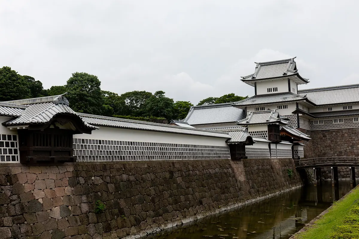 White lattice walls and turrets of Kanazawa Castle above a stone wall and moat