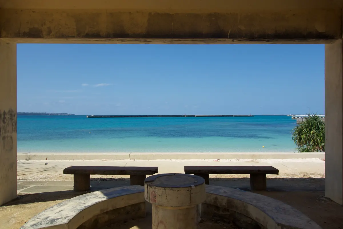 View of the turquoise sea and a breakwater from a shaded beach shelter with benches in Miyako Island, Okinawa