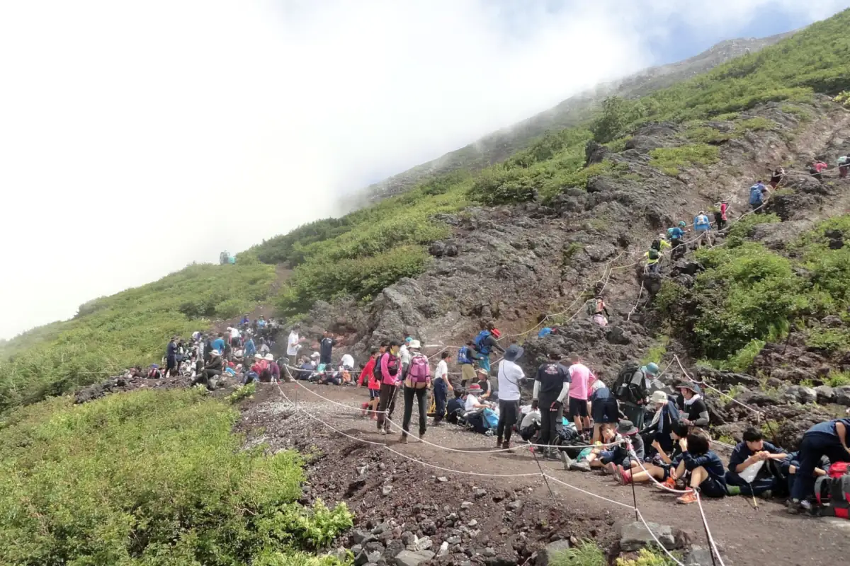Many climbers resting and walking along the rope-lined Yoshida Trail on Mount Fuji's volcanic slope
