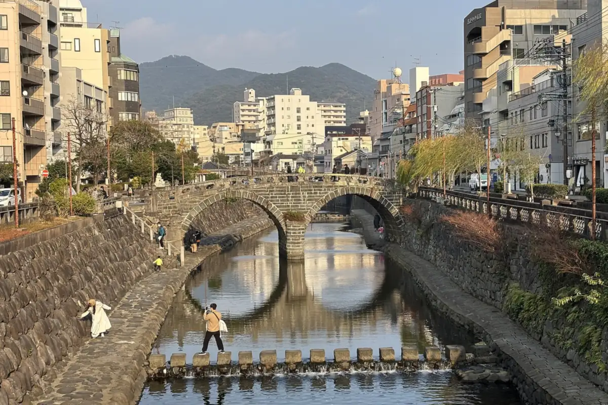 長崎の川に映る眼鏡橋の2つの石のアーチと、石畳の岸を歩く人々