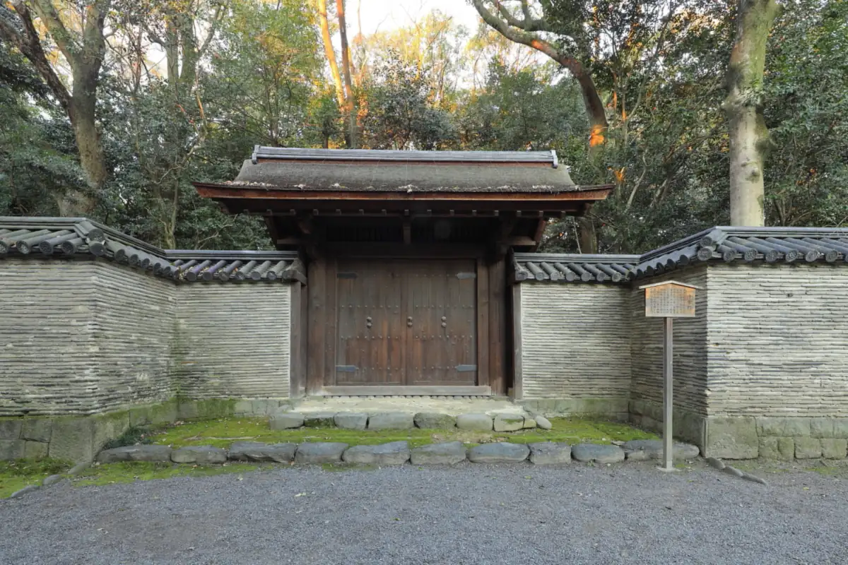 Wooden Seisetsumon gate with a tiled roof between long gray walls at Atsuta Jingu