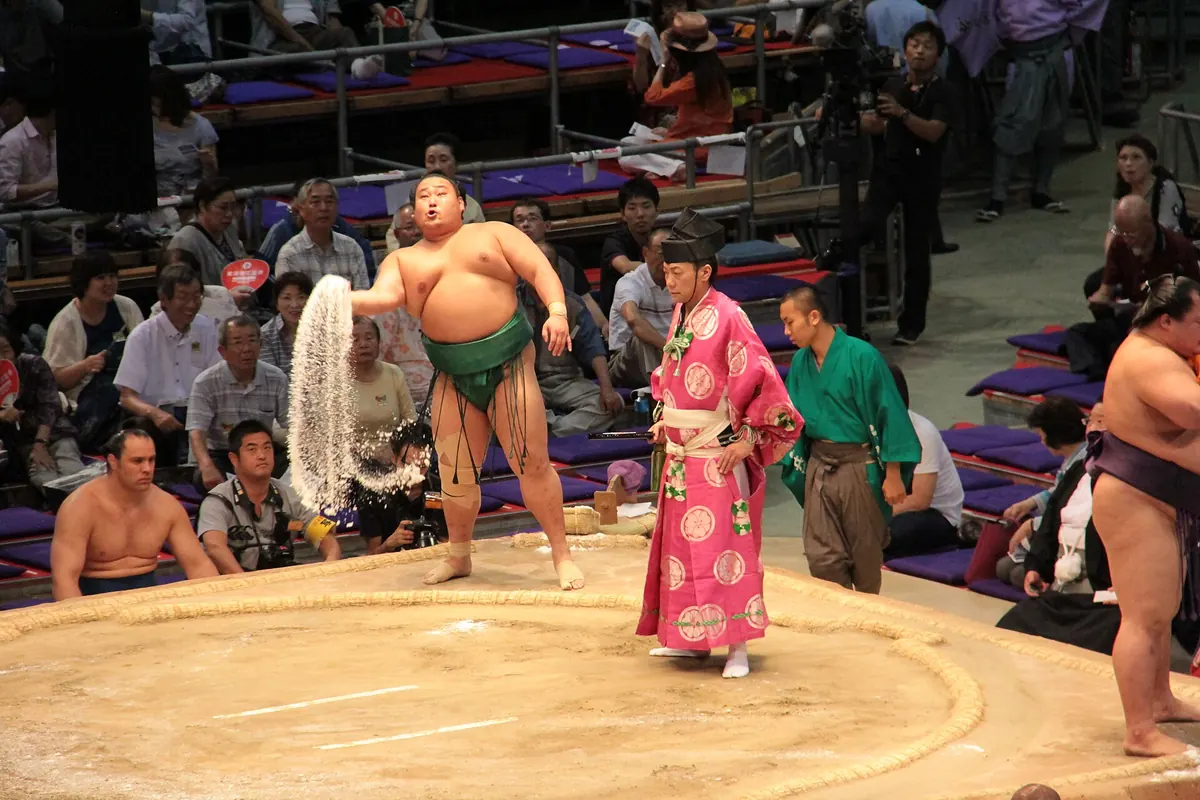 Sumo wrestler throwing salt into the ring in Nagoya, with a referee in a pink robe and spectators in the seats