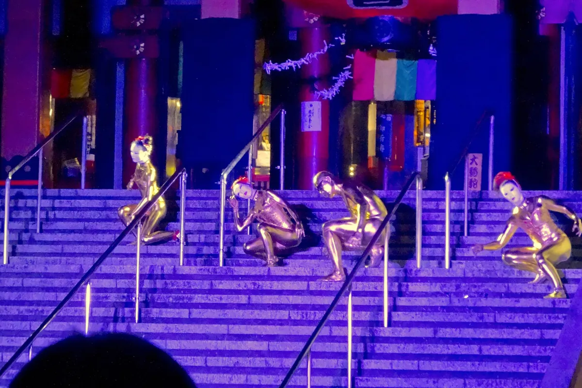 Gold-painted street performers posing on temple steps at night during Nagoya's Osu Street Performers Festival