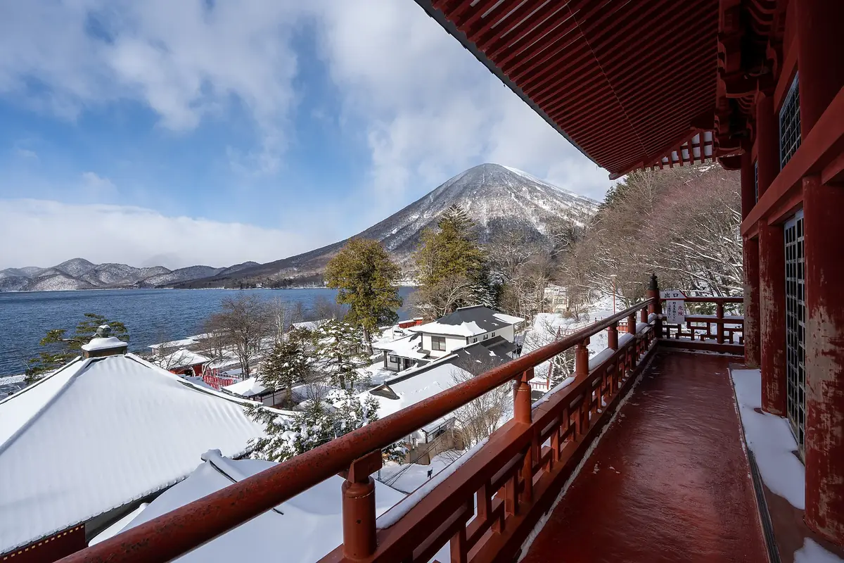 A red-railed balcony overlooking snow-covered roofs, Lake Chuzenji and a snow-capped mountain in Nikko