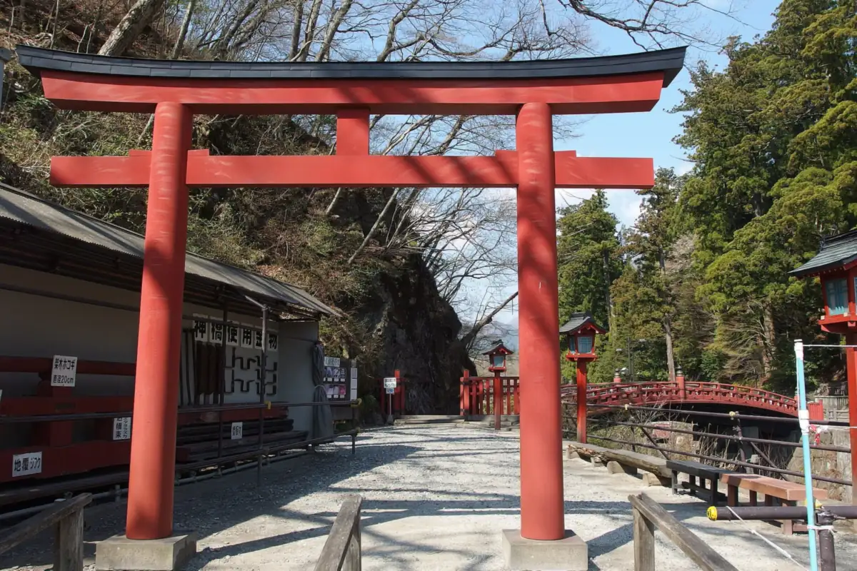 A red torii of Futarasan Shrine and the red Shinkyo Bridge in Nikko, surrounded by bare trees and rocky cliffs