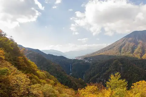 닛코 산비탈에 펼쳐진 노란색과 주황색 단풍, 그 뒤로 보이는 게곤 폭포, 난타이산, 주젠지호