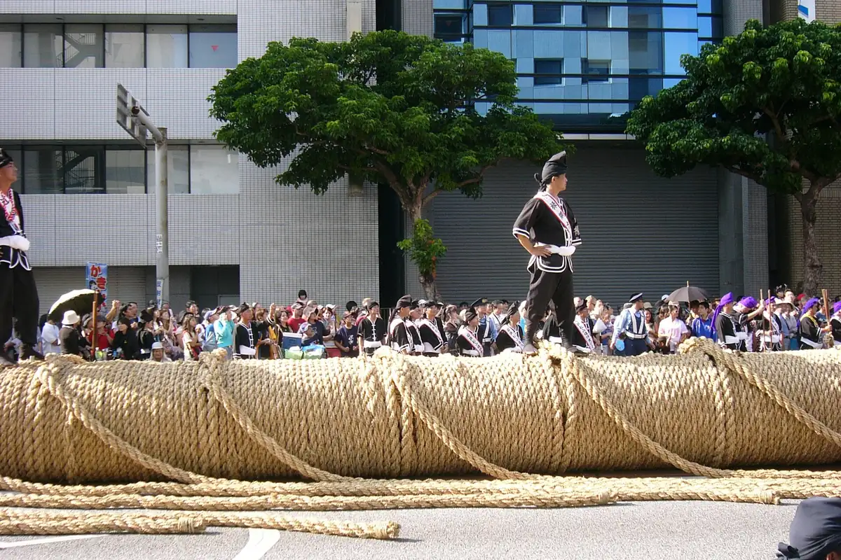 People in black costumes stand on a giant tug-of-war rope at the Naha Matsuri, with a crowd lined up behind it