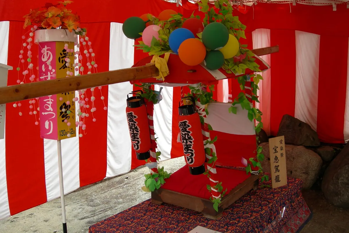 A hoekago palanquin decorated with balloons and green leaves against red-and-white curtains at Aizen Matsuri in Osaka