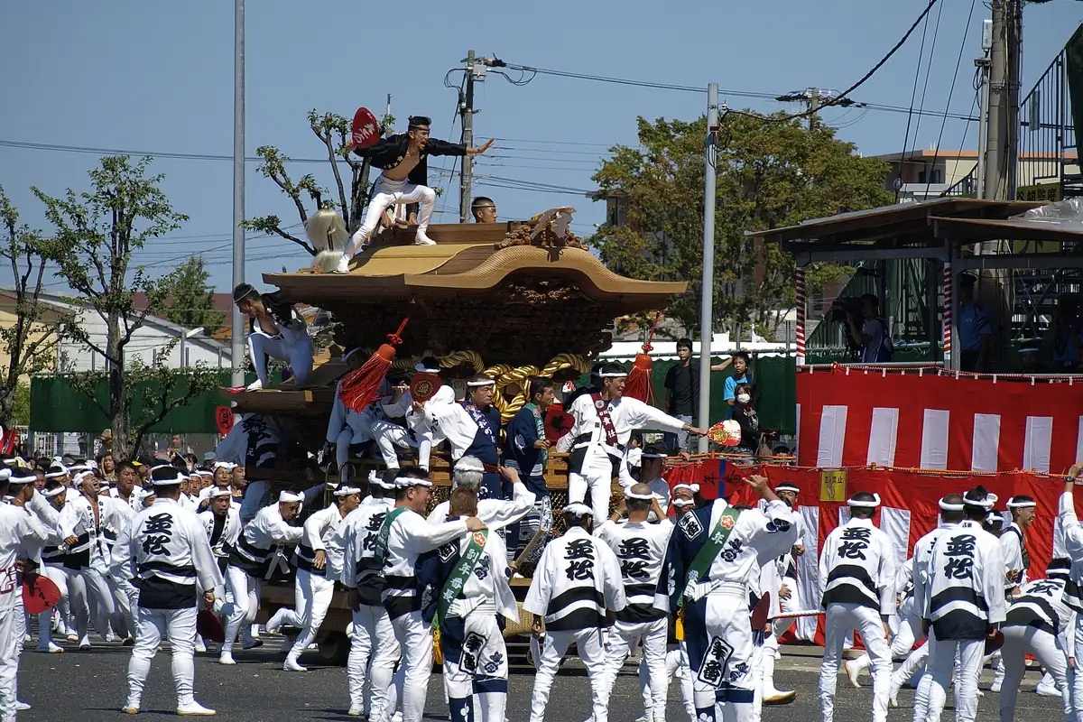 Men in white and black happi coats pulling a danjiri float with a curved roof through a street in Kishiwada