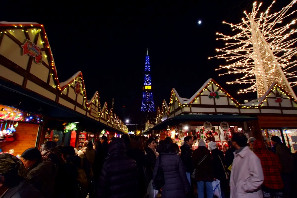 Crowds walk between the stalls of the Munich Christmas Market in Odori Park, Sapporo, with the TV Tower lit up behind