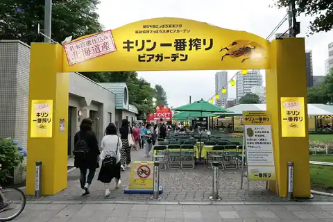 노란색 비어가든 입구 아치 아래를 걷는 사람들, 뒤로 보이는 초록 파라솔과 테이블