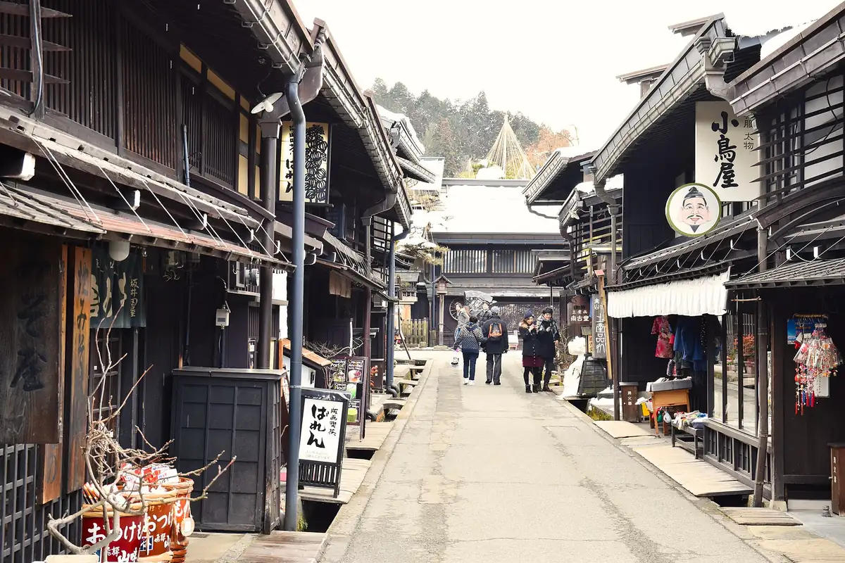 Dark wooden houses and shop signs lining a narrow street in Takayama's old town, with a few people walking