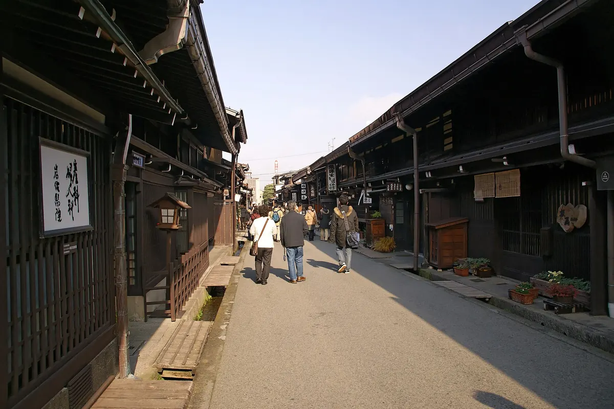 Long street of dark wooden machiya houses in Sanmachi, Takayama, with a few people walking