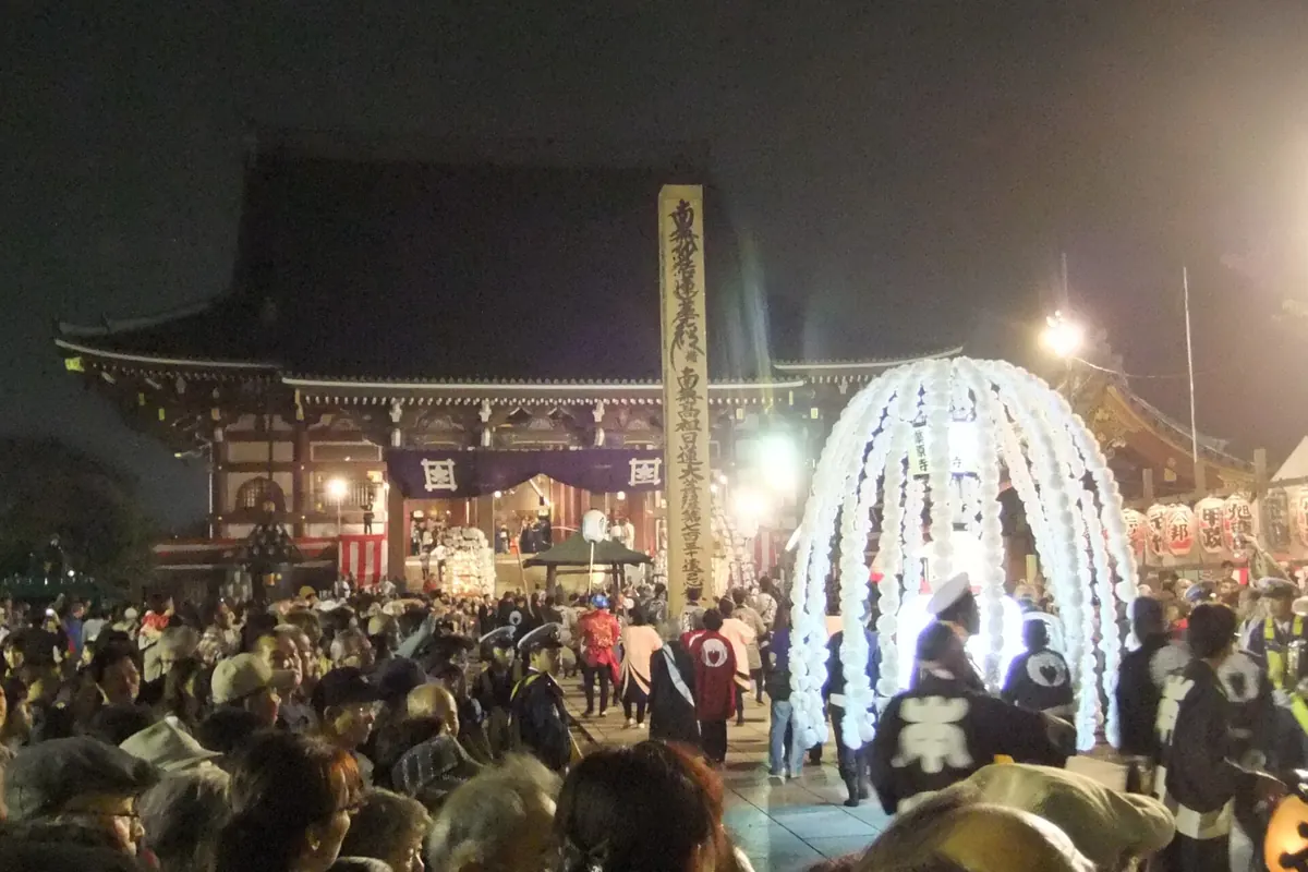 本門寺前のお会式で、白く光る提灯の飾りのそばに集まる夜の人々