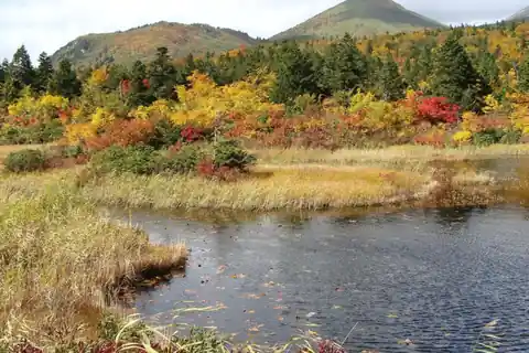 Red and yellow autumn leaves around Suirennuma pond with the Hakkoda mountains in the background, Aomori