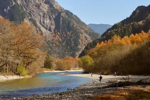Autumn foliage along the Azusa River in the Kamikochi valley, with visitors on the gravel banks