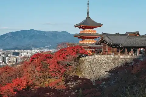 Three-story pagoda of Kiyomizu-dera in Kyoto, with red autumn maples in front and the city and mountains beyond