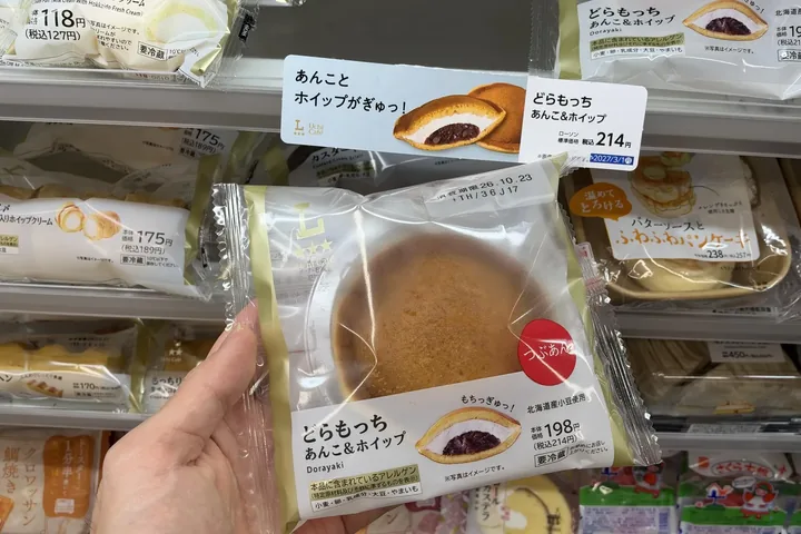 A Dora-mocchi with red bean paste and whipped cream held at a Lawson in Tokyo on 20 October 2026; the shelf tag reads 214 yen with tax