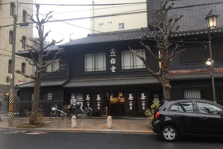 The black wooden front of Ippodo Tea's main store in Kyoto, with noren curtains reading 茶 and 一保堂, bicycles parked outside