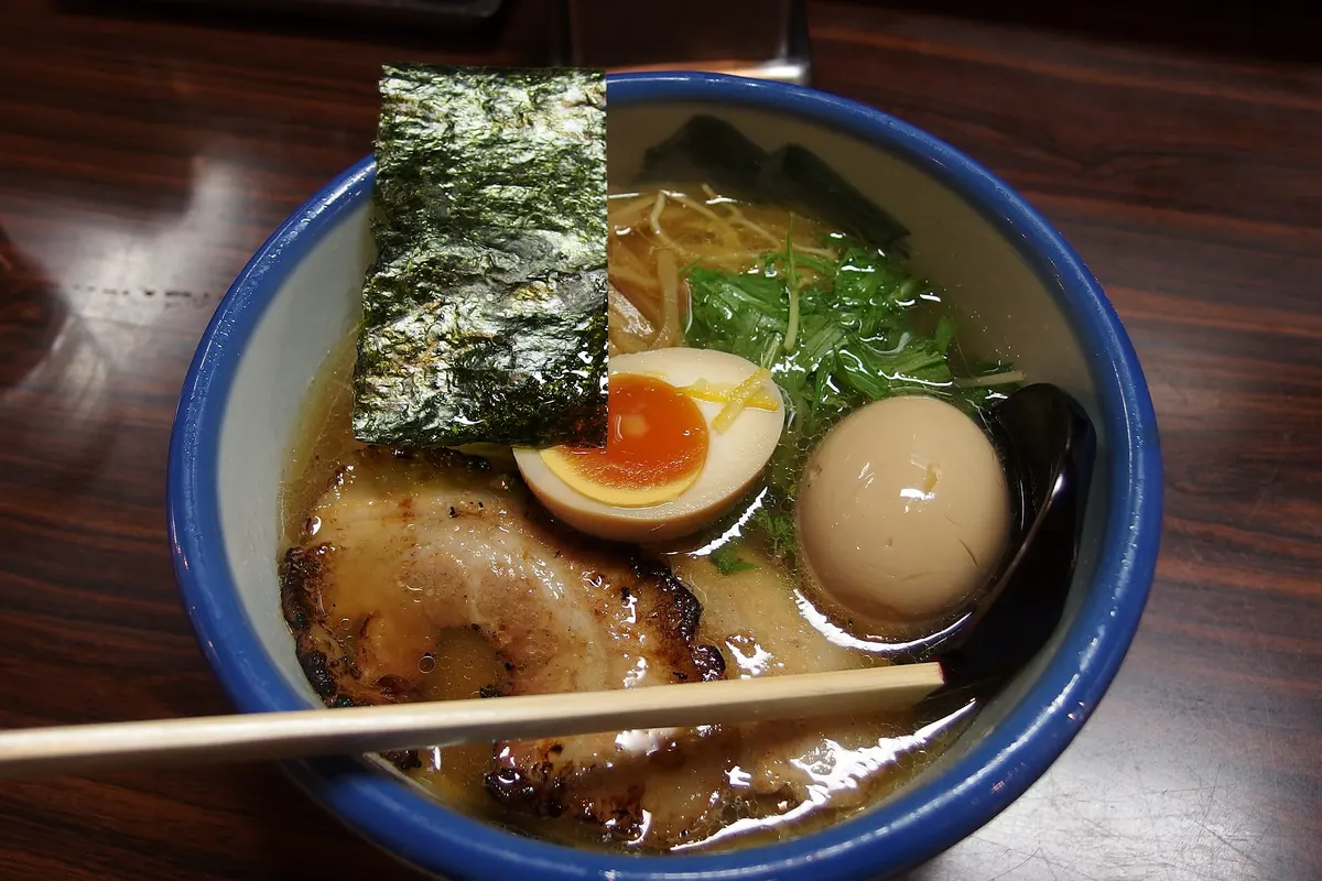 Bowl of Afuri yuzu shio ramen with nori, a halved soft-boiled egg, pork slices, and greens in a blue-rimmed bowl