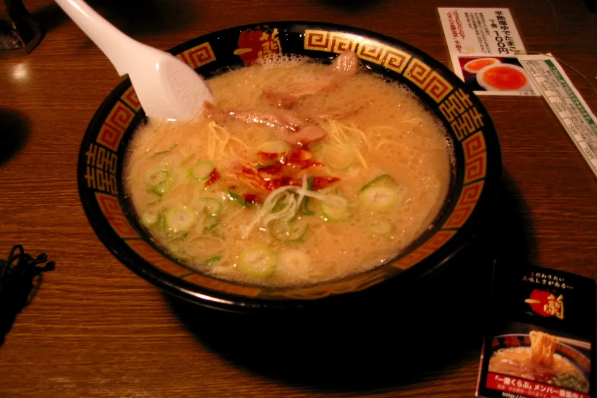 Bowl of Ichiran tonkotsu ramen with a red chili topping and a white spoon in the signature red-rimmed black bowl