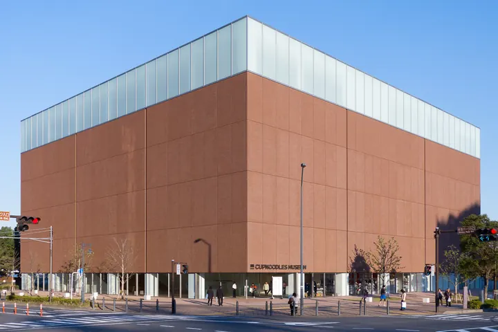 Exterior of the CUPNOODLES MUSEUM building in Yokohama with a glass upper floor and people near the entrance