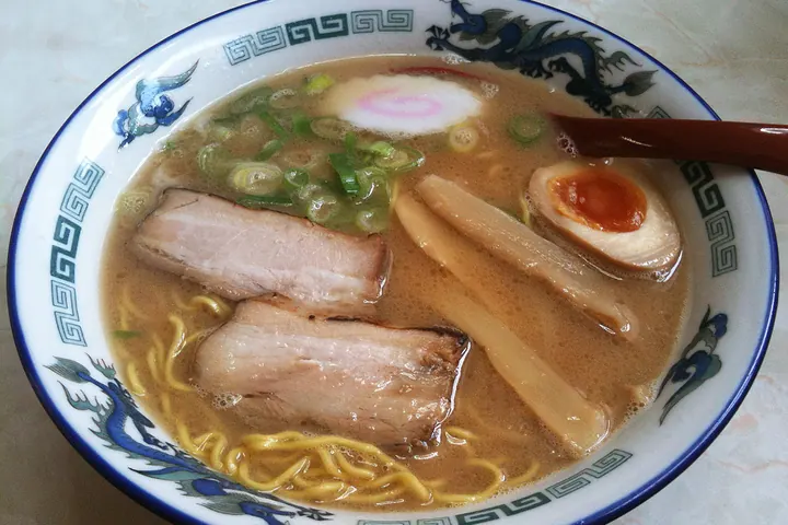 Bowl of shoyu ramen with chashu pork, narutomaki, bamboo shoots, and a soft-boiled egg in a dragon-patterned bowl in Asahikaw