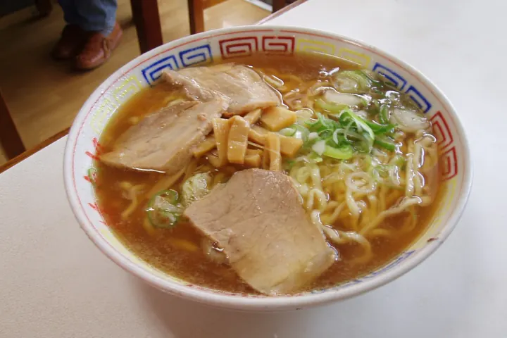 Bowl of Kitakata ramen with thick curly noodles, chashu pork, bamboo shoots, and scallions in brown broth