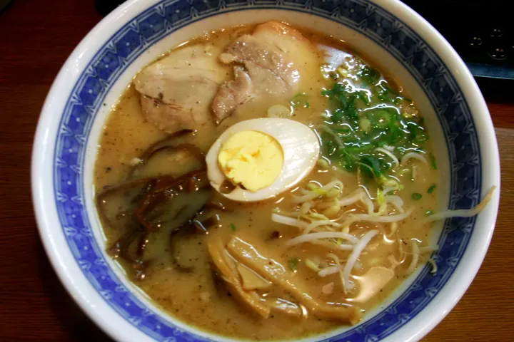 Bowl of Kumamoto tonkotsu ramen with dark broth, chashu pork, a soft-boiled egg, bean sprouts, and greens