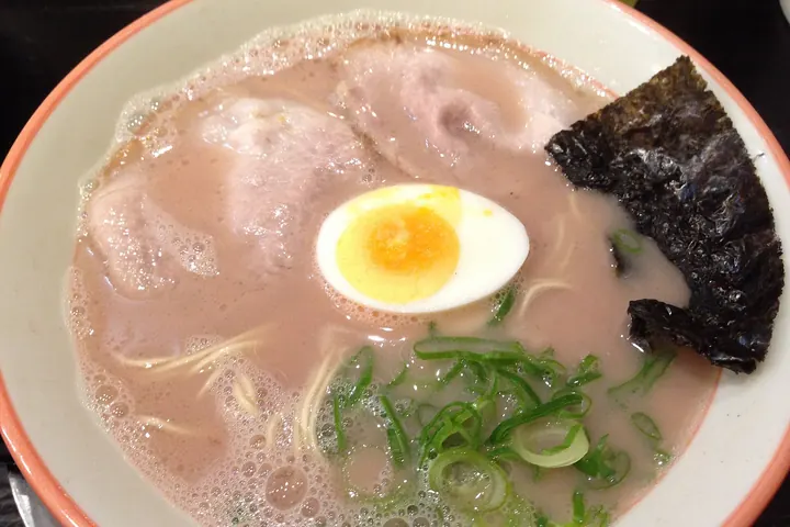 A bowl of tonkotsu ramen with sliced pork, a half boiled egg, nori, and scallions in cloudy pork-bone broth