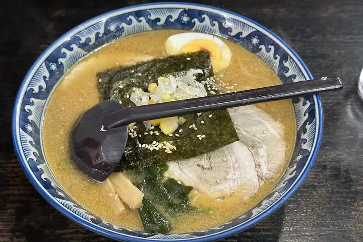 A bowl of miso ramen with pork, nori, a boiled egg, bean sprouts, corn, and bamboo shoots in a blue patterned bowl