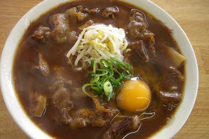 Bowl of Tokushima ramen in dark broth with thin sliced pork, bean sprouts, scallions, and a raw egg yolk