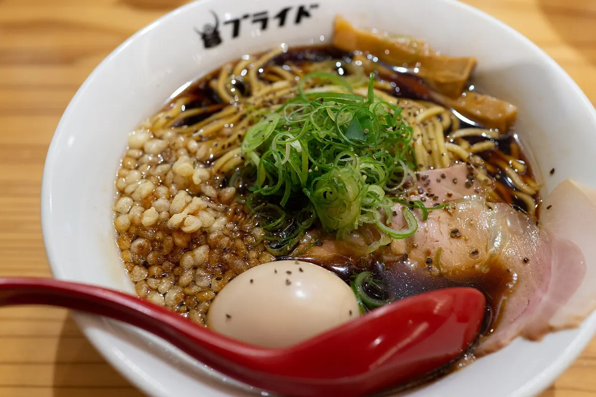 Bowl of Toyama Black ramen in dark broth with noodles, pork, bamboo shoots, scallions and a soft-boiled egg
