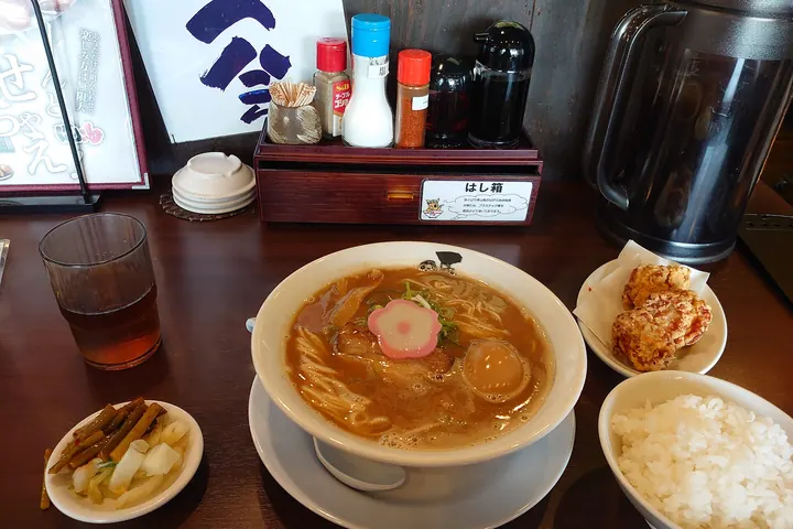 Wakayama ramen in brown broth with pork, narutomaki, and a soft egg, served with rice, pickles, and fried chicken