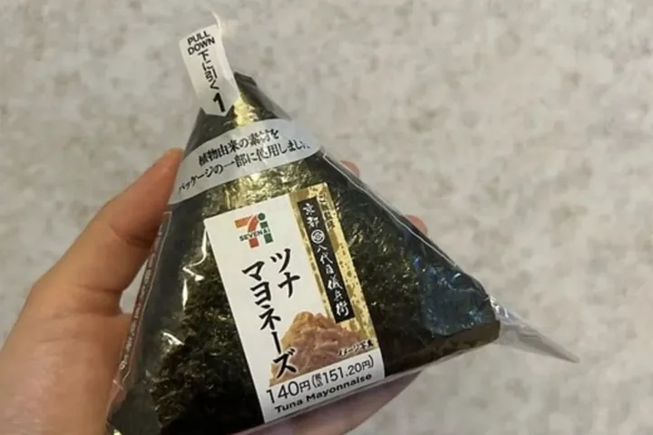 A tuna mayonnaise onigiri from 7-Eleven held in a hand; the label reads 140 yen