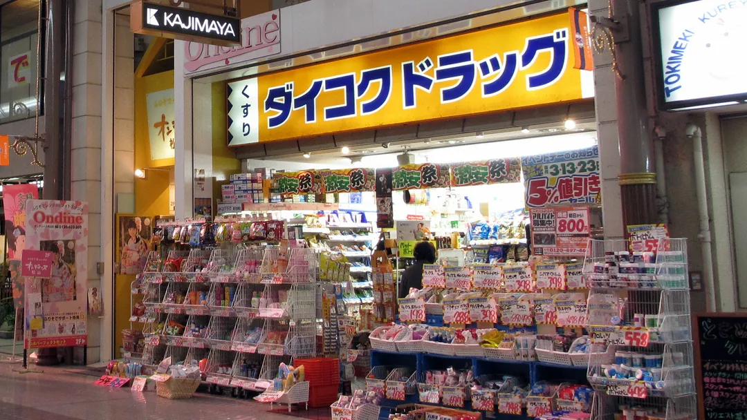 爱媛县松山市商店街里的大国药妆(Daikoku Drug)店面,店门口摆满商品货架的照片